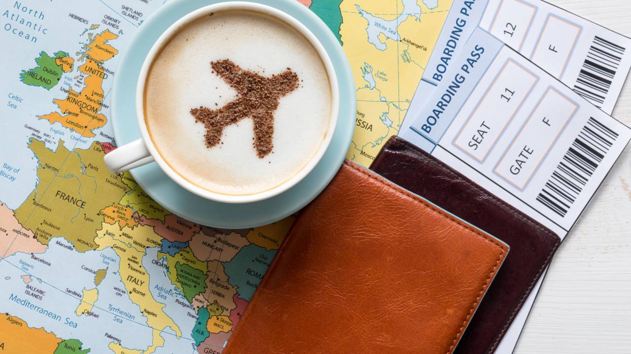 fotografia de uma xícara de café em cima de um mapa que mostra a Europa, ao lado de passagens de avião