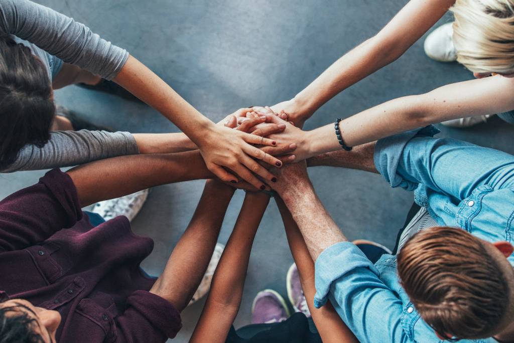 Um grupo de pessoas se reúne em círculo e juntam suas mãos, mostrando colaboração em equipe