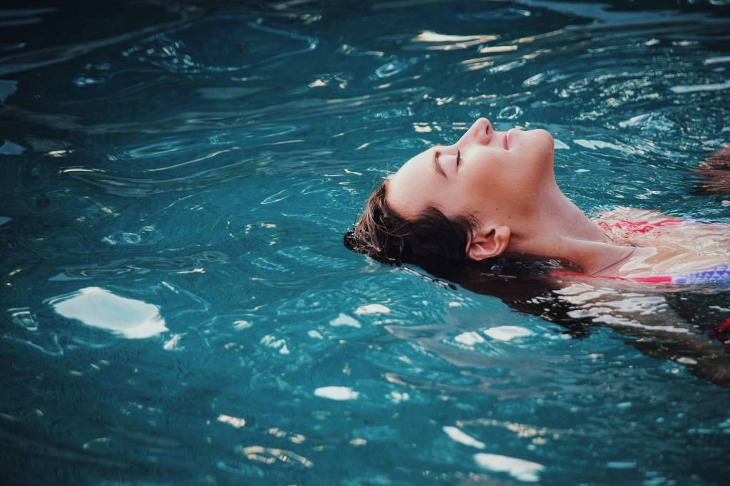 Imagem mostra o rosto de uma mulher branca que está boiando numa piscina.