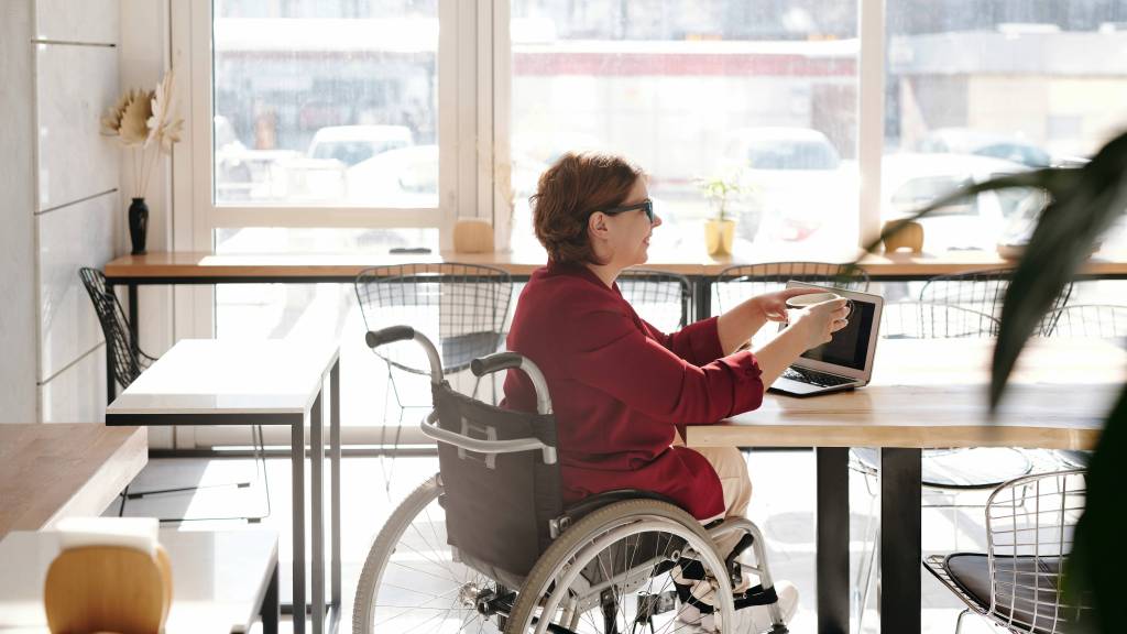 Imagem mostra uma mulher branca de cabelos curtos e óculos em uma cadeira de rodas