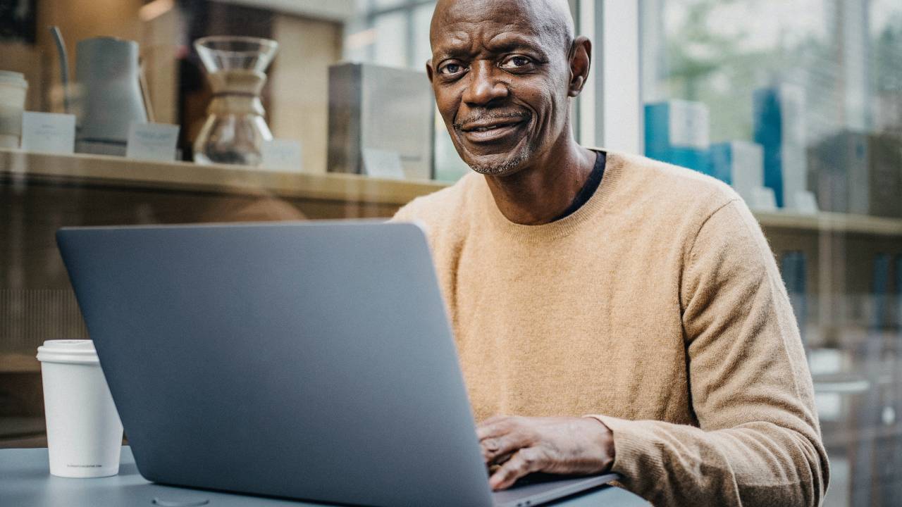 Um homem negro de aproximadamente 50 anos aparece trabalhando no computador.