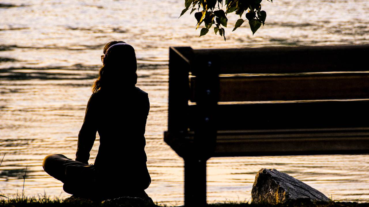Foto de mulher meditando em frente a um lago.