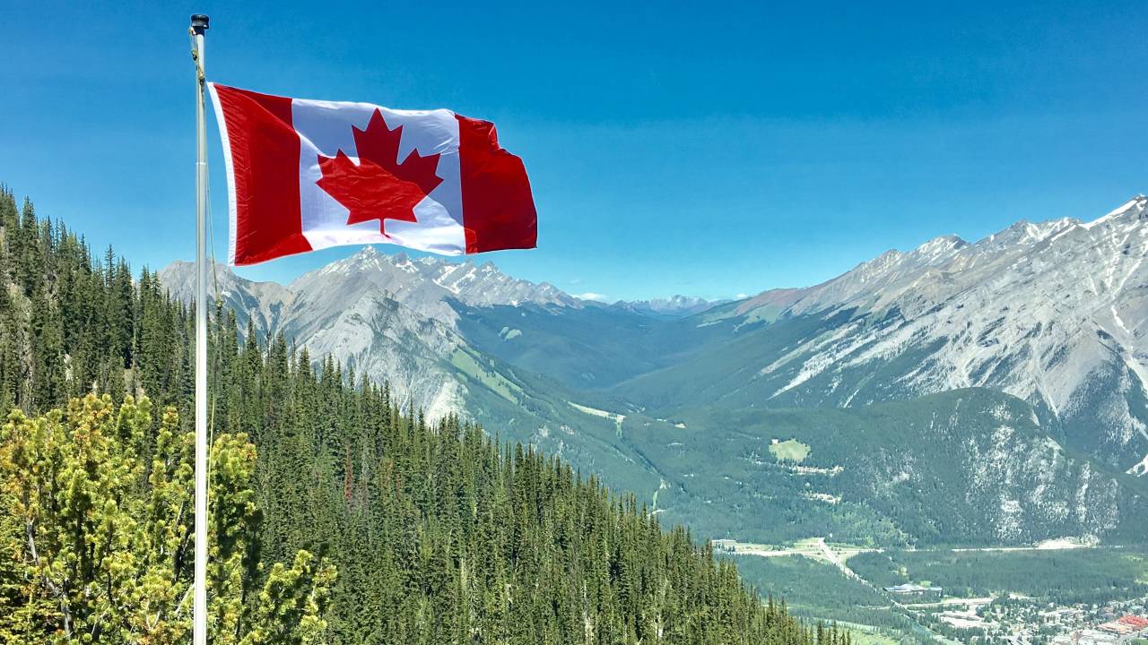 Bandeira do Canadá em frente a montanhas e floresta.