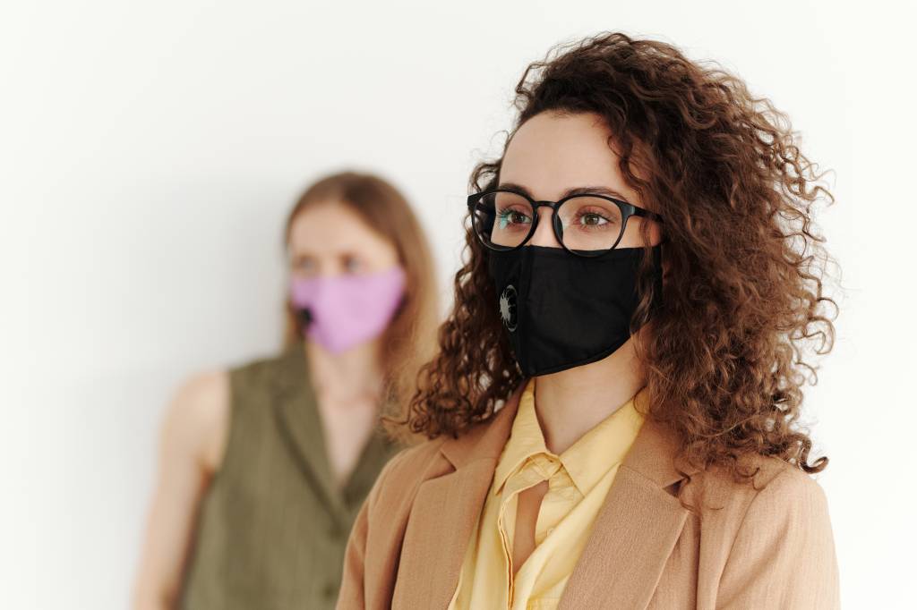 Duas mulheres aparecem na imagem usando máscara e vestindo traje social.
