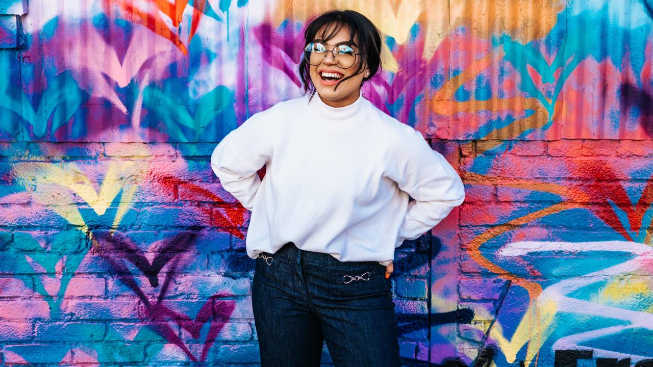 Mulher sorrindo em frente a um muro colorido.