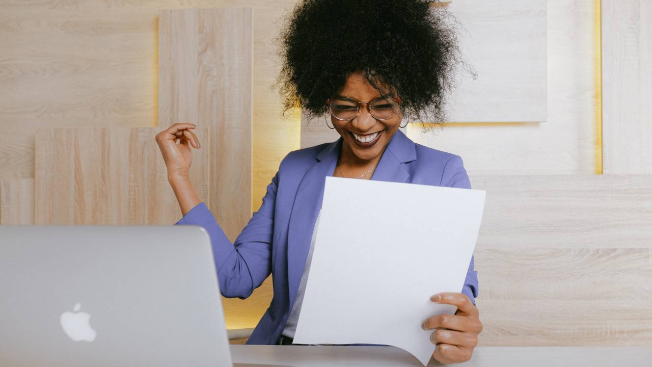 Mulher negra sorrindo ao ler um documento.