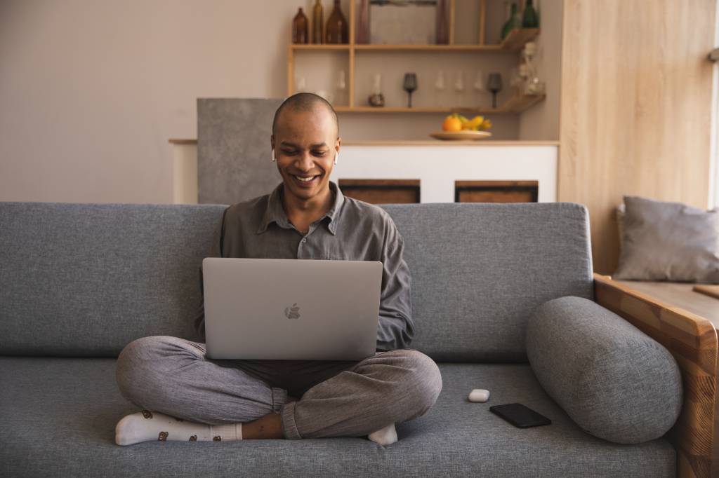 Um homem aparece sentado no sofá sorrindo enquanto usa o computador.