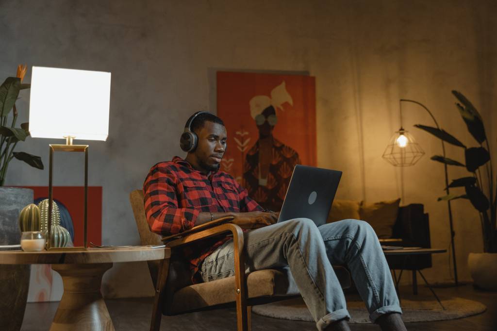 Homem negro em casa usando notebook e fone de ouvido.