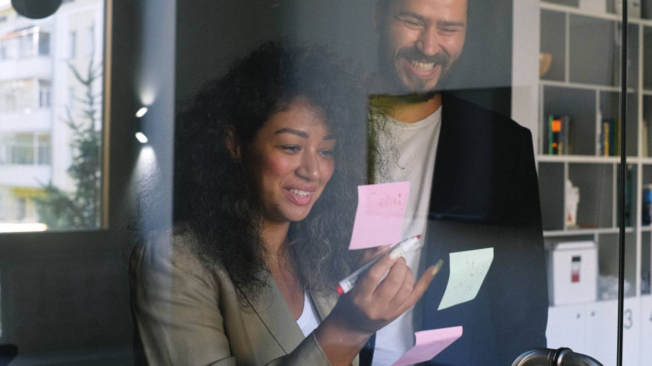 Um homem e uma mulher aparecem verificando post-its colados em um vidro.