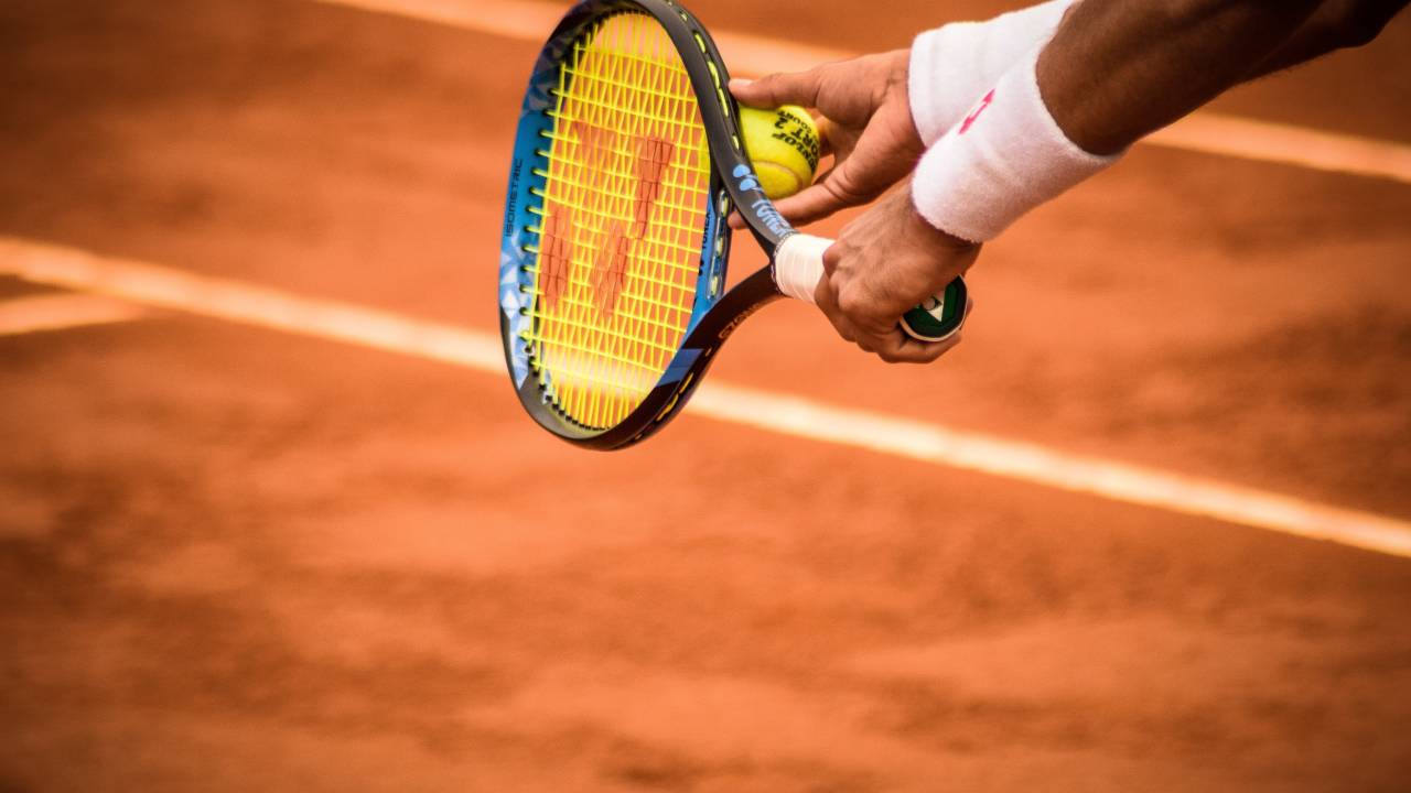 A foto mostra mãos de um tenista que irá sacar a bola de tênis.