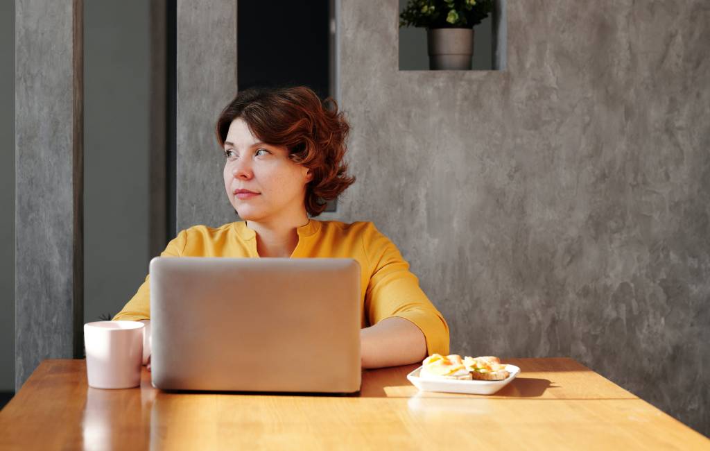 Uma mulher aparece olhando para o lado direito, enquanto usa o computador.