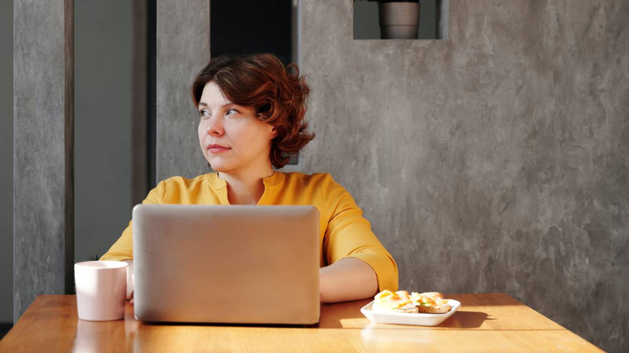 Uma mulher aparece olhando para o lado direito, enquanto usa o computador.