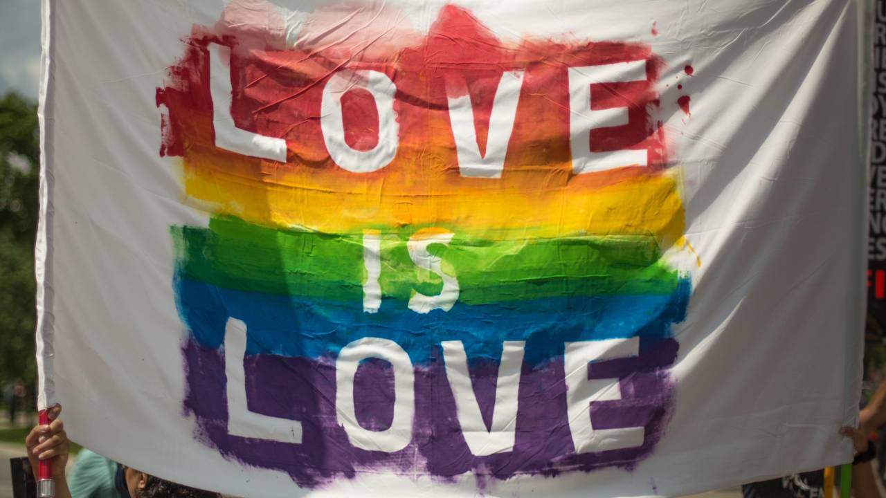 Uma bandeira com as cores do arco íris aparece com os dizeres: "love is love".