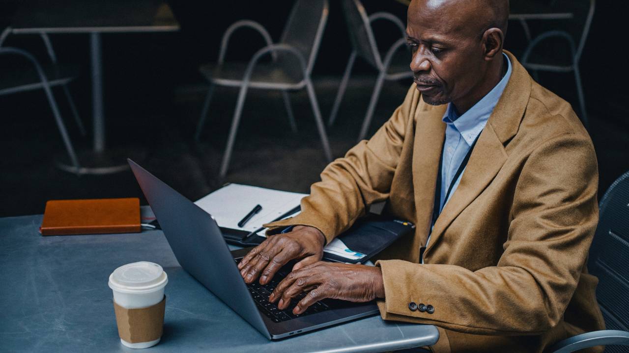 A foto mostra um homem negro por volta de 50 anos trabalhando em um notebook