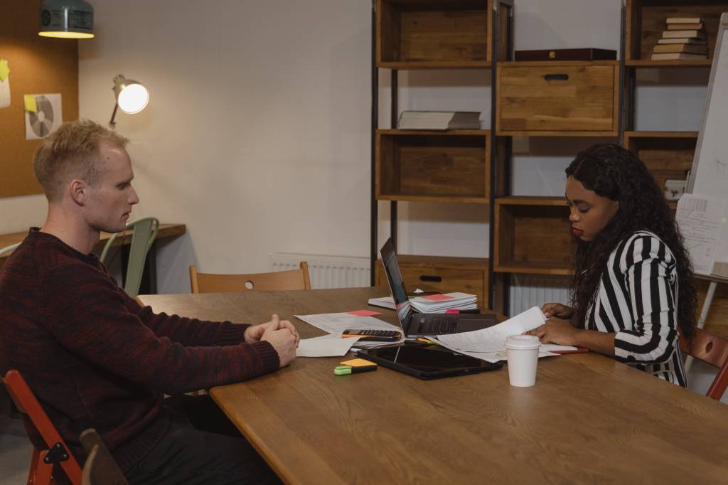 Uma mulher negra entrevista um homem loiro em um escritório