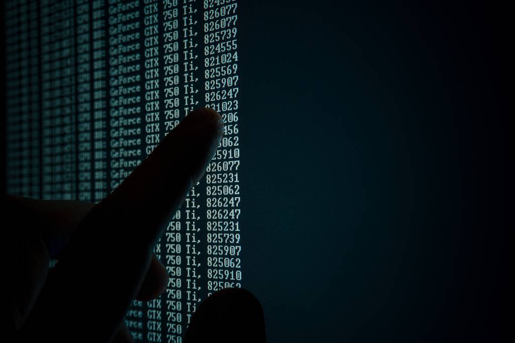 Mão apontando uma tela de computador com dados numéricos;