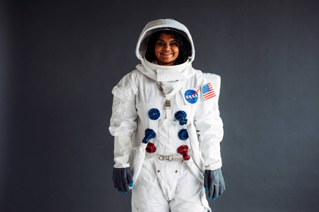 Uma mulher aparece usando um traje de astronauta com um logo da Nasa.
