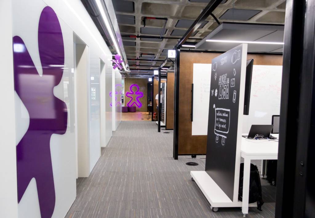 Imagem mostra o escritório da Vivo, com o símbolo da empresa em roxo nas paredes.
