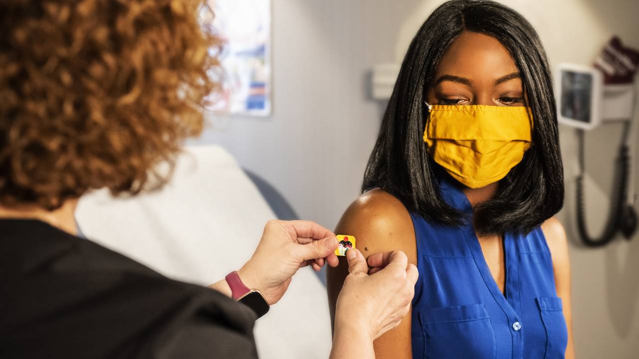 Imagem mostra uma mulher negra recebendo um band-aid no braço após a vacinação