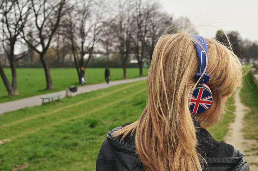 Imagem mostra uma mulher loira de costas usando fones de ouvido com o desenho da bandeira do Reino Unido.