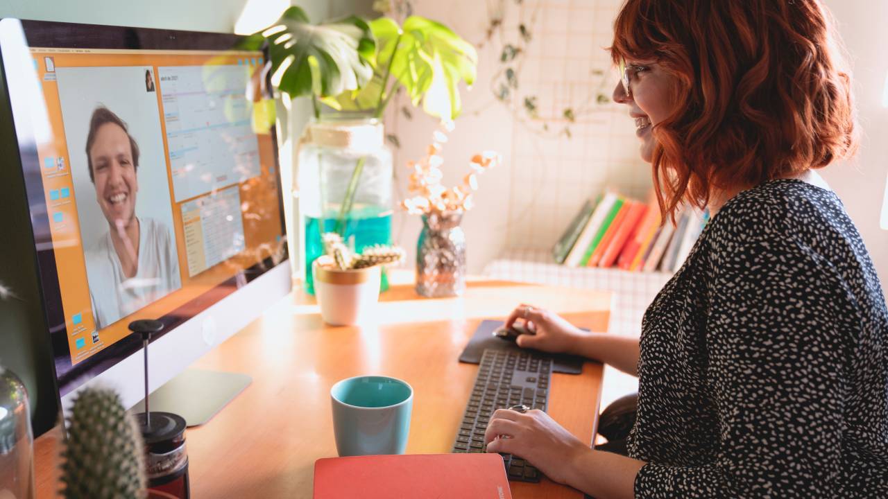 Imagem mostra mulher branca de cabelos ruivos conversando com um homem branco em uma videoconferência on computador.