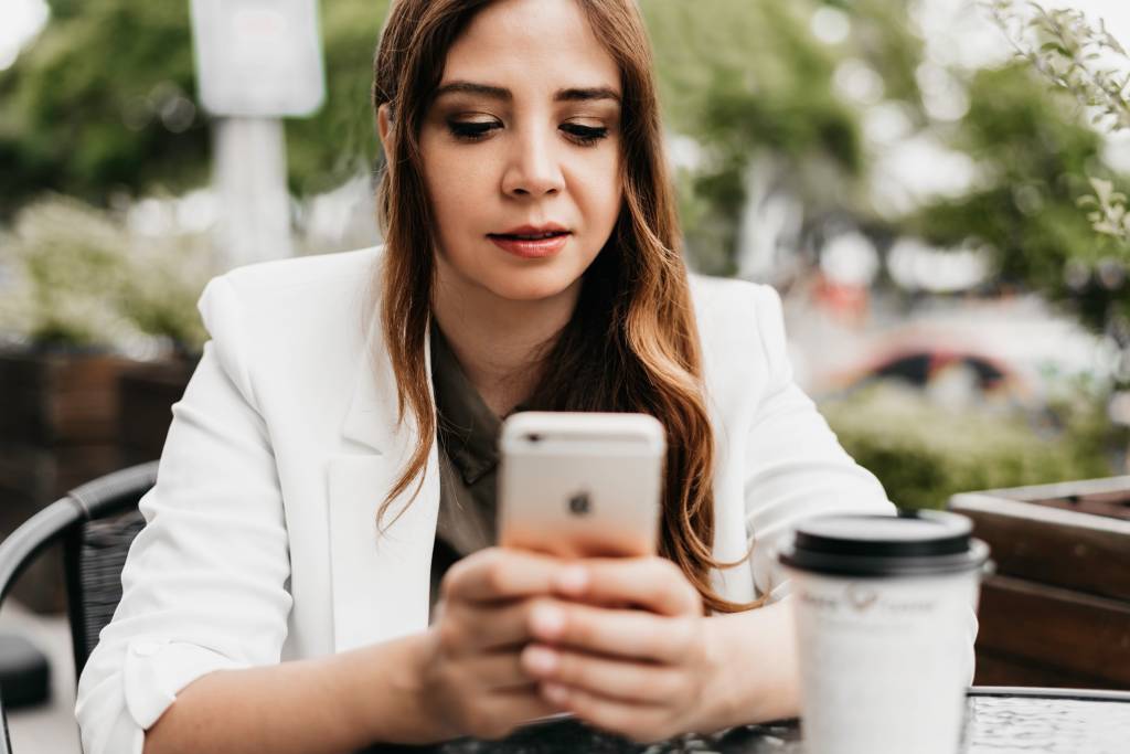 Imagem mostra uma mulher jovem, branca, de cabelos castanhos, olhando preocupada para o celular
