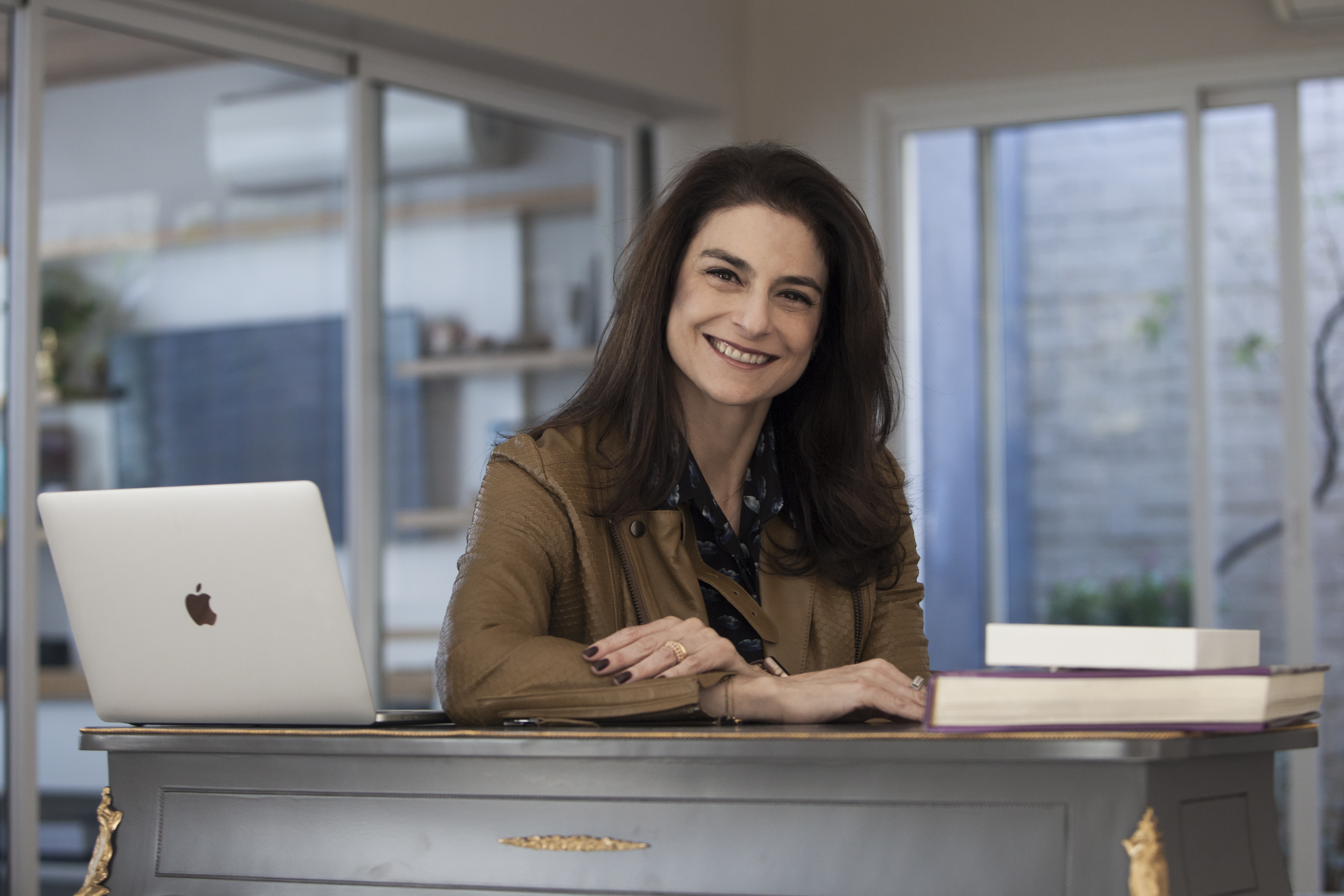 Foto de Francine Graci, uma mulher branca, de cabelos castanhos, sorrindo sentada em uma mesa