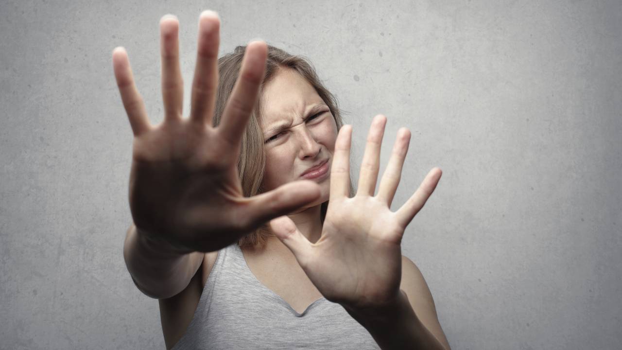 Imagem mostra uma mulher loira com as mãos na frente do rosto, em um gesto de impedir que alguém se aproxime