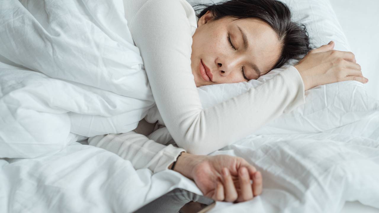 Imagem mostra uma mulher oriental dormindo em uma cama com edredom branco