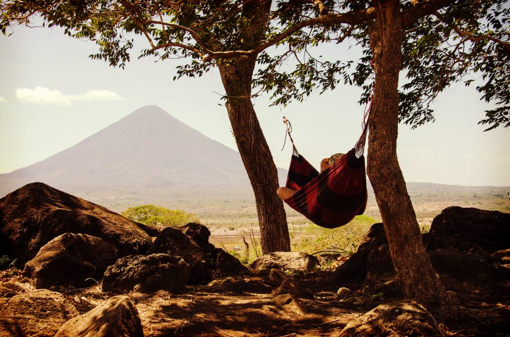 Mulher descansa em rede entre duas árvores com vista para as montanhas