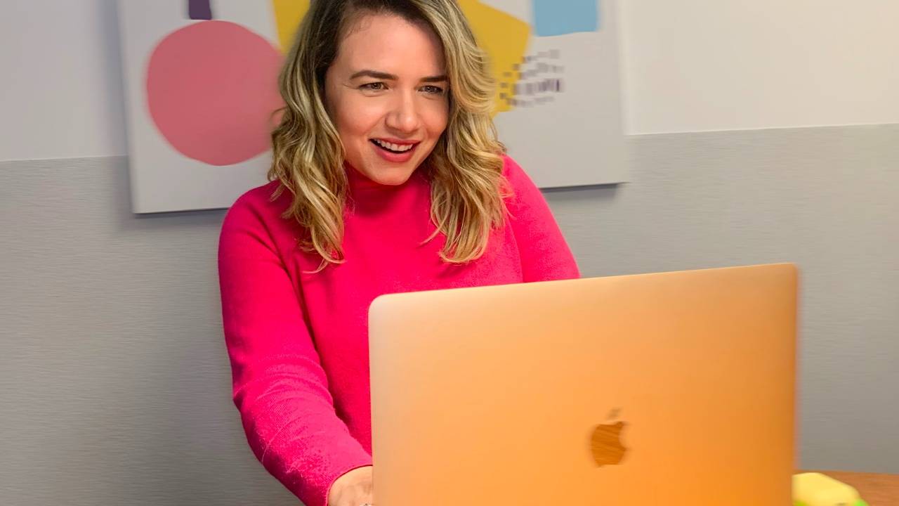 Imagem mostra a CEO da Jobecam, Cammila Yochabell, sorrindo enquanto olha para um notebook.