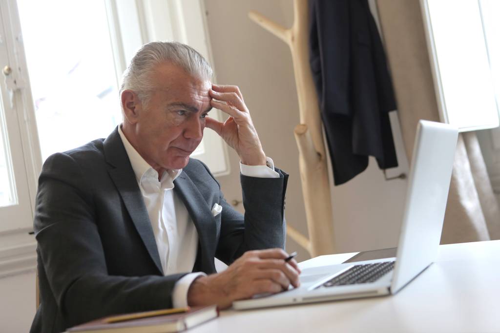 Imagem mostra um homem branco de cabelos grisalhos com semblante preocupado olhando o notebook