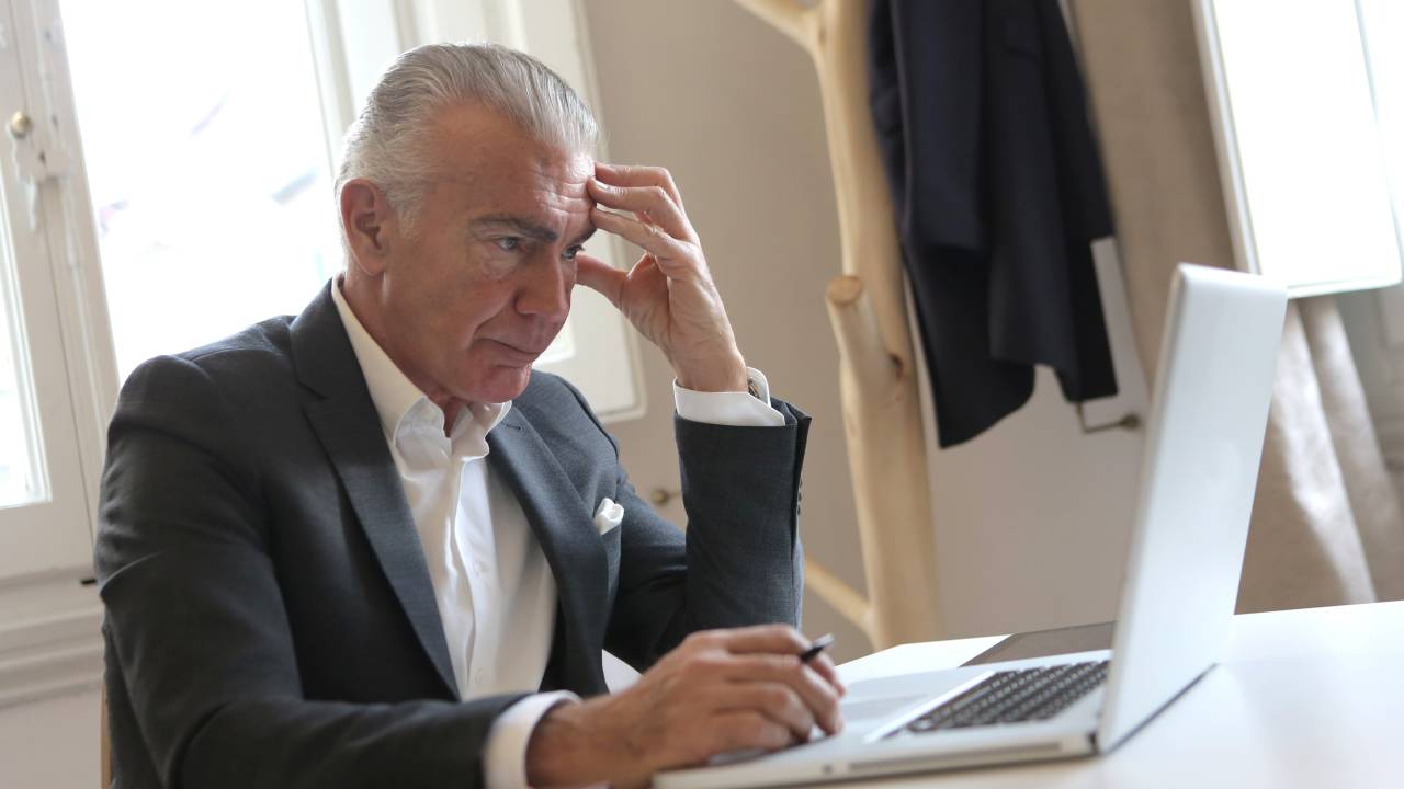 Imagem mostra um homem branco de cabelos grisalhos com semblante preocupado olhando o notebook