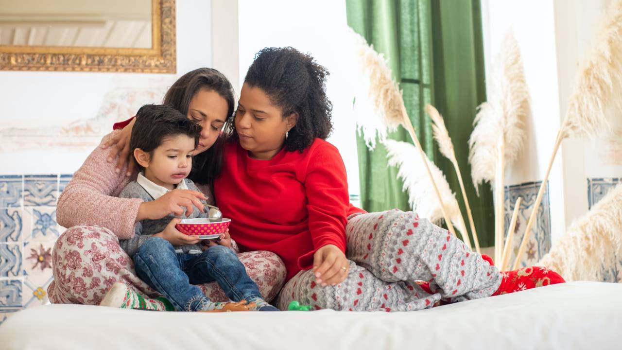 Imagem mostra duas mulheres juntas, uma delas está com uma criança no colo enquanto a alimenta.