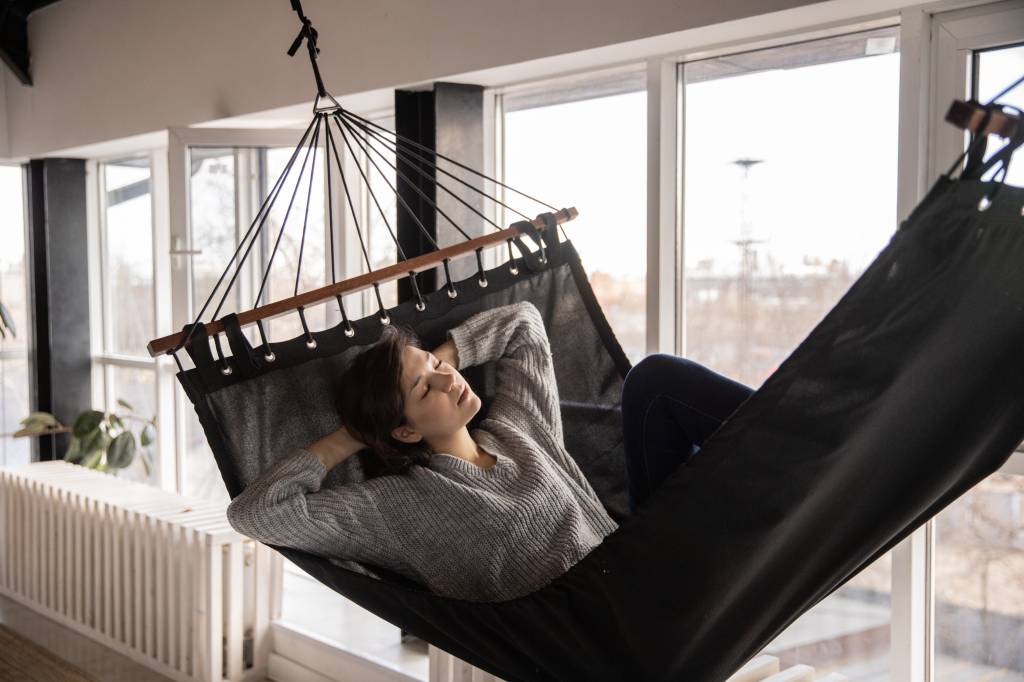Imagem mostra uma mulher jovem deitada em uma rede, cochilando