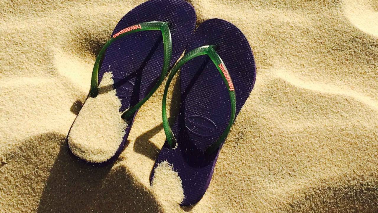 Foto de um par de havaianas azuis em cima da areia