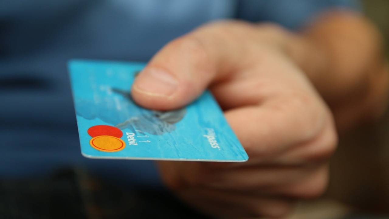 Foto mostra a mão de uma pessoa segurando um cartão de crédito azul.