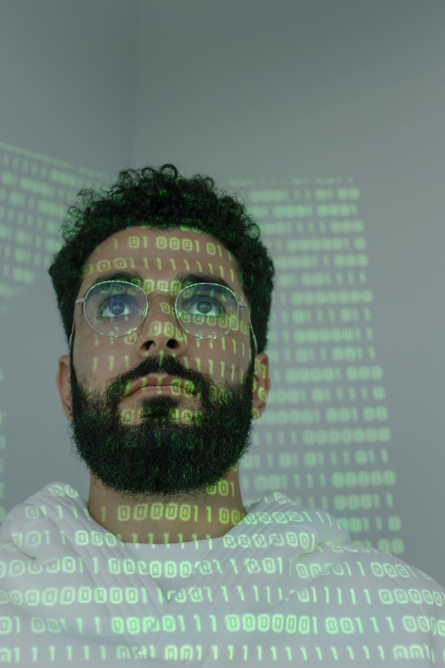 Imagem mostra o rosto de um homem olhando para uma tela. Em seu rosto, estão refletidos dados que estão na tela.