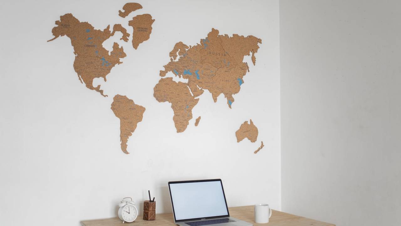 Imagem mostra uma mesa de home office. Na parede, está um mapa-múndi.