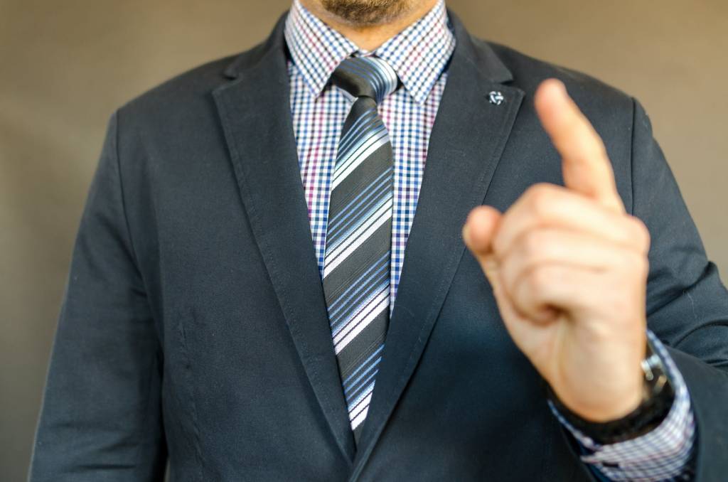 Homem de terno e gravata aponta o dedo em direção à câmera