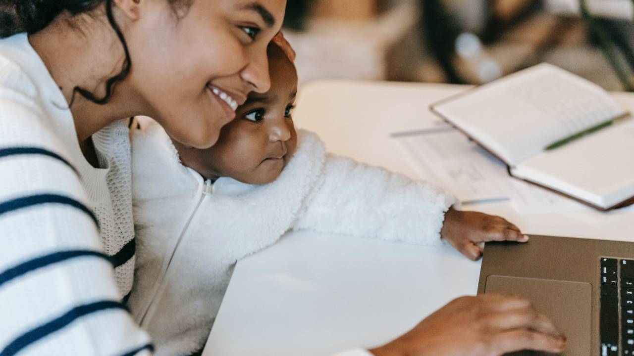 Uma mulher com um bebê no colo olham para a tela de um notebook