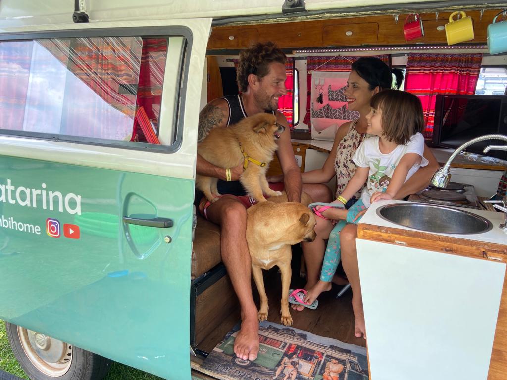 Natália, seu marido, Aleandro, e sua filha, Lorena, estão dentro da Kombi com dois cachorros de cor caramelo