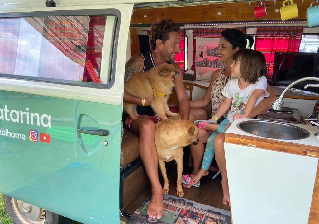 Natália, seu marido, Aleandro, e sua filha, Lorena, estão dentro da Kombi com dois cachorros de cor caramelo