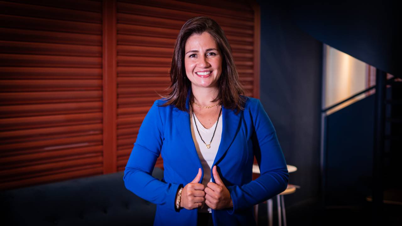 Mariana Dias, CEO da Gupy, veste um blazer azul com uma camiseta branca por baixo. Ela sorri para a foto