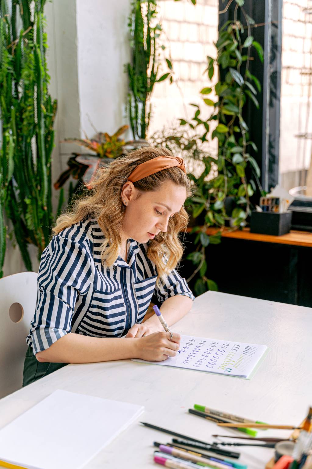 Uma mulher está sentada enquanto olha para um caderno, concentrada, e segura um lápis