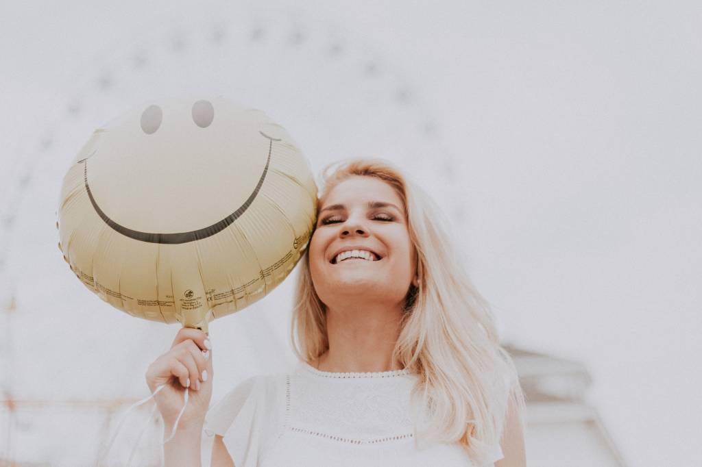 Mulher sorrindo segura um balão com o emoji smile