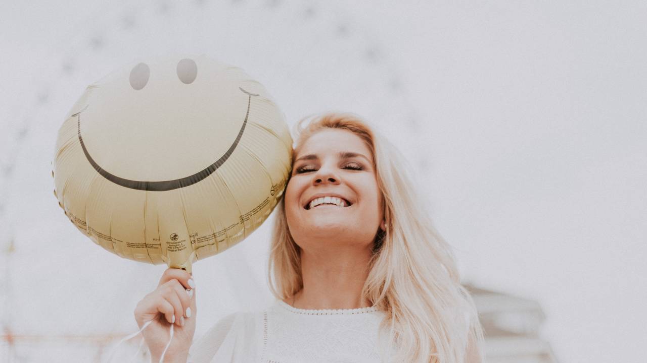 Mulher sorrindo segura um balão com o emoji smile