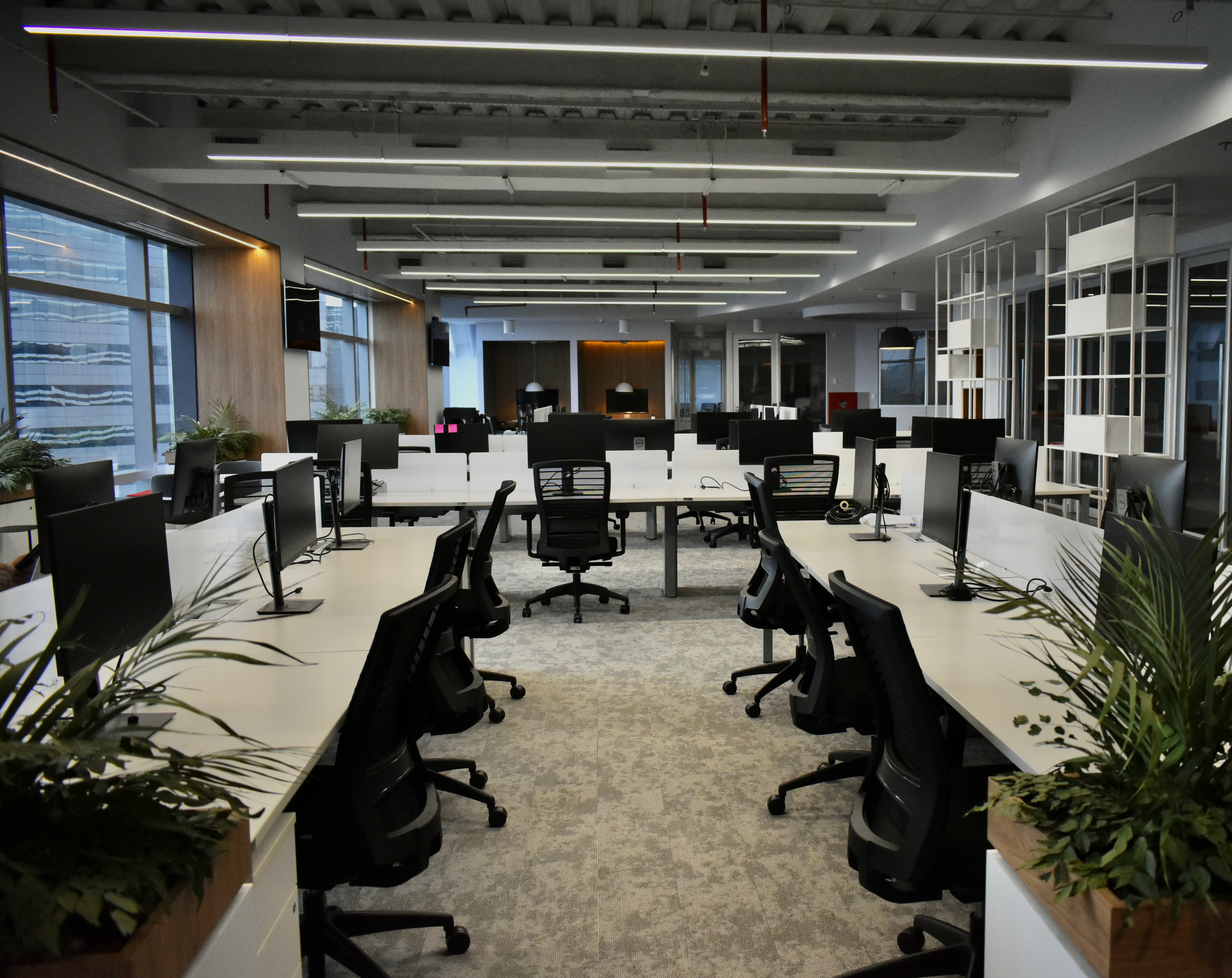 Foto mostra um dos espaços do novo escritório da Audi. Esse espaço, que tem carpete de pano claro, várias mesas de escritório estão dispostas, mas nenhuma delas é fixa