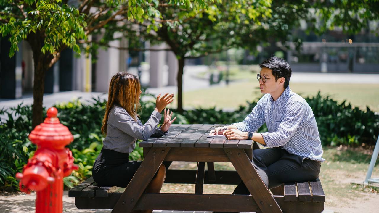 Mulher e homem conversam em uma mesa ao ar livre