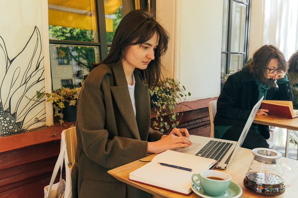 Mulher com sobretudo trabalha em um notebook em um café